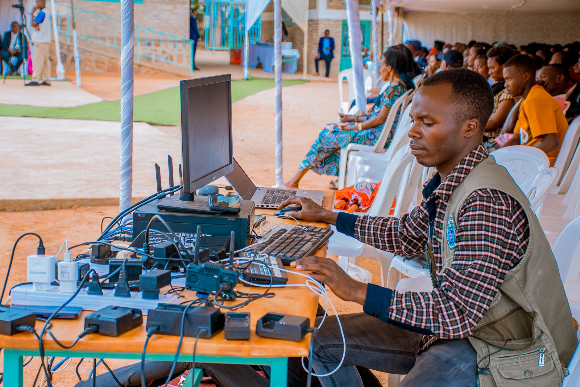 Technician managing electrical and computer setup at an outdoor event with attentive audience. — Preparing the Next Generatio