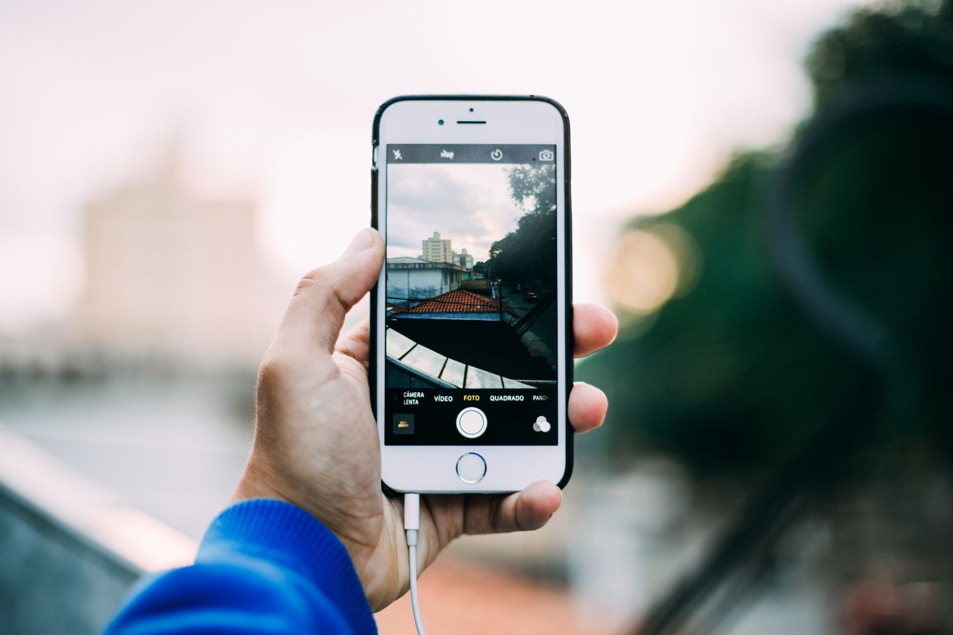 Close-up of a hand holding a smartphone while capturing a cityscape outdoors. — Technology Redundancy and Reliability in Emer